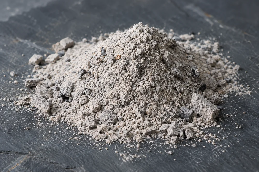 A small pile of pale grey biomass ash on dark slate
