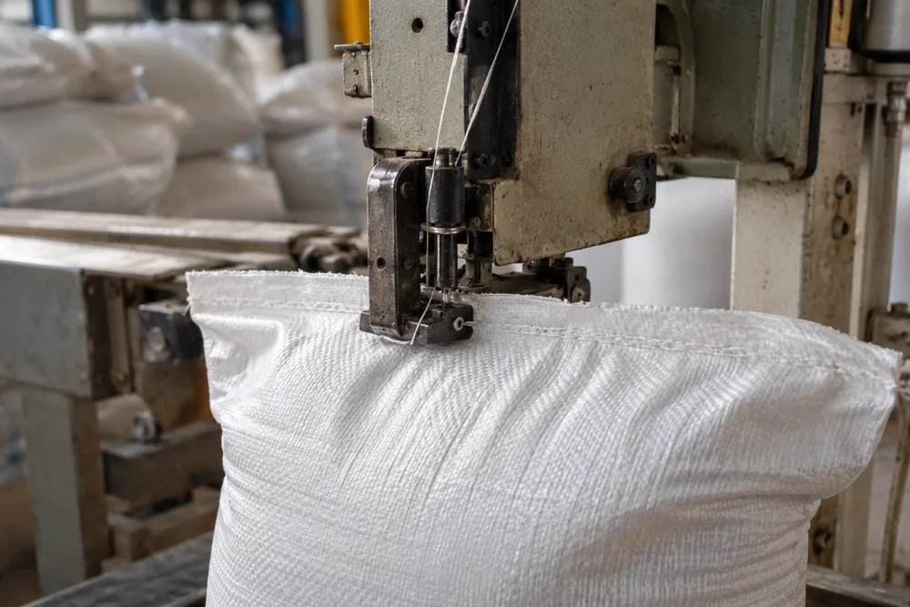 Filled white sack being closed by a bag-stitching machine